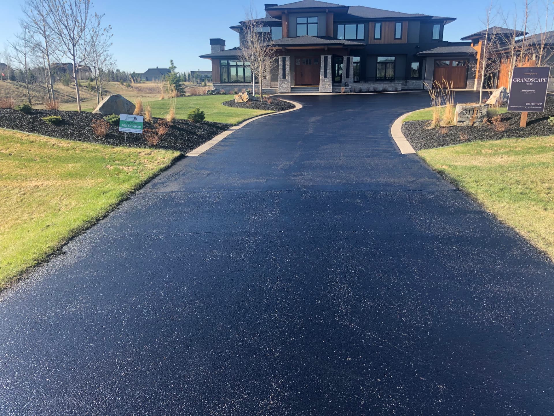 Freshly sealed black asphalt driveway leading to the double garage of a Calgary family home